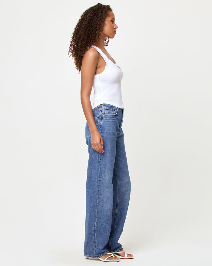 Side view of a model wearing the LSPACE Ash Tank in muah, a white cropped ribbed racerback tank with a rhinestone lips graphic, styled with medium wash blue wide-leg jeans and white sandals.