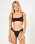 Front view of a model wearing the LSPACE black Effie Bikini Top, a ribbed bralette-style top with wide straps and a ruched center front, paired with matching black ribbed bikini bottoms on a neutral background.