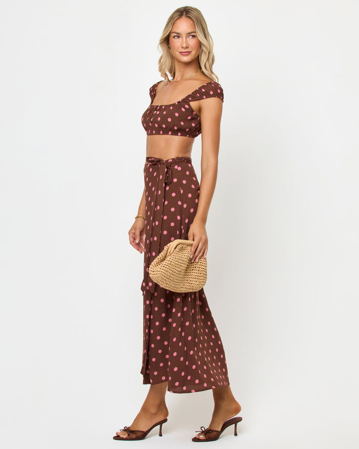 Side view of a model wearing the LSPACE Ever Top in alotta polka dot, showing the brown and pink polka dot cap-sleeve crop top with the matching wrap skirt.