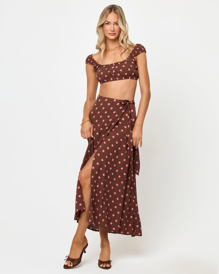 Front view of a model wearing the LSPACE Ever Top in alotta polka dot, showing the brown and pink polka dot cap-sleeve crop top and the side-tie detail on the matching wrap skirt.