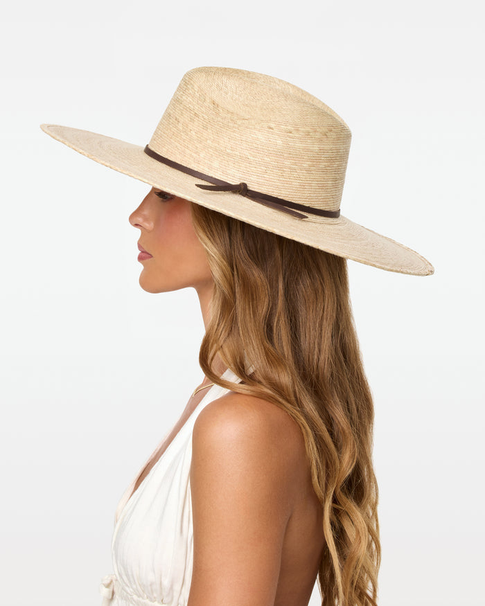 Side profile view of a model wearing the natural Isla Hat with a white halter top, showing the wide brim and dark cord band detail.