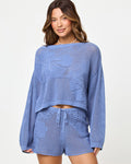 Close-up of a model wearing the LSPACE Island Time Sweater in Chambray, styled with the matching Island Time Short, highlighting the open-knit crochet floral design and long sleeves.