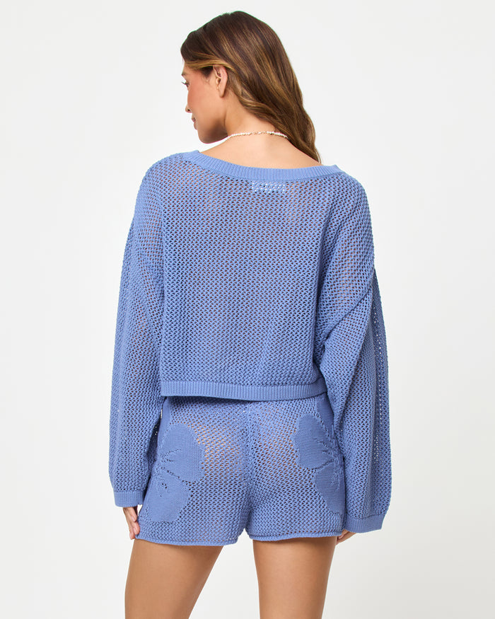 Back view of a model wearing the LSPACE Island Time Sweater in Chambray, styled with the matching Island Time Short, showing the open-knit crochet construction and relaxed fit.