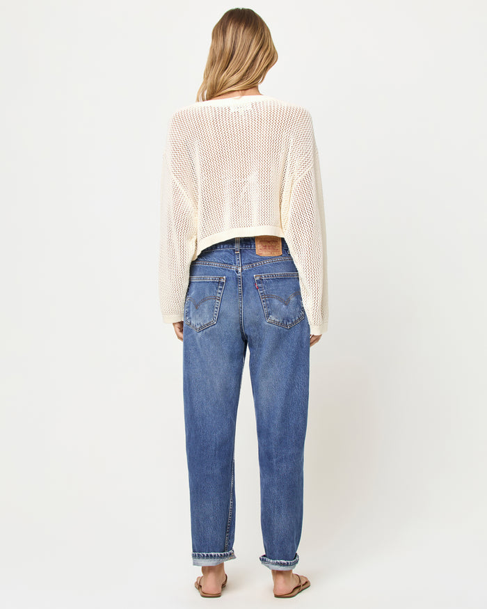 Back view of a model wearing the LSPACE Island Time Sweater in Cream, styled with jeans, showing the open-knit crochet construction and relaxed fit.