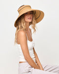 Side view of a model wearing the natural and black Jess Roll Up Hat with a white tank top and grey sweatpants, seated.