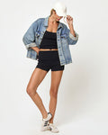 Full-length front view of a model wearing the LSPACE Leigh Tank and Short in black, an oversized denim jacket, white sneakers, and a white cap.