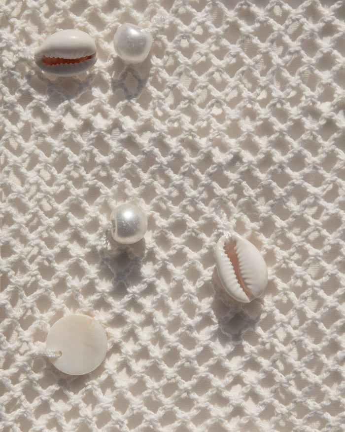 Close-up of cream open-knit crochet fabric with natural shell embellishments.