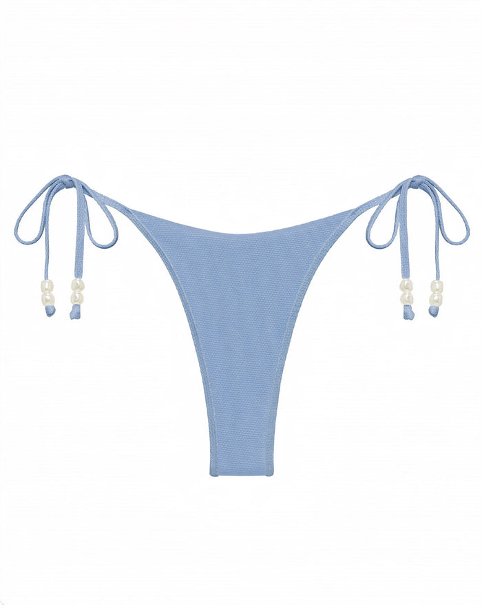 Off-model flat lay of the LSPACE chambray Lucia Bikini Bottom showing the double side ties with pearl bead accents, styled with a matching Sunrise Shell bikini top