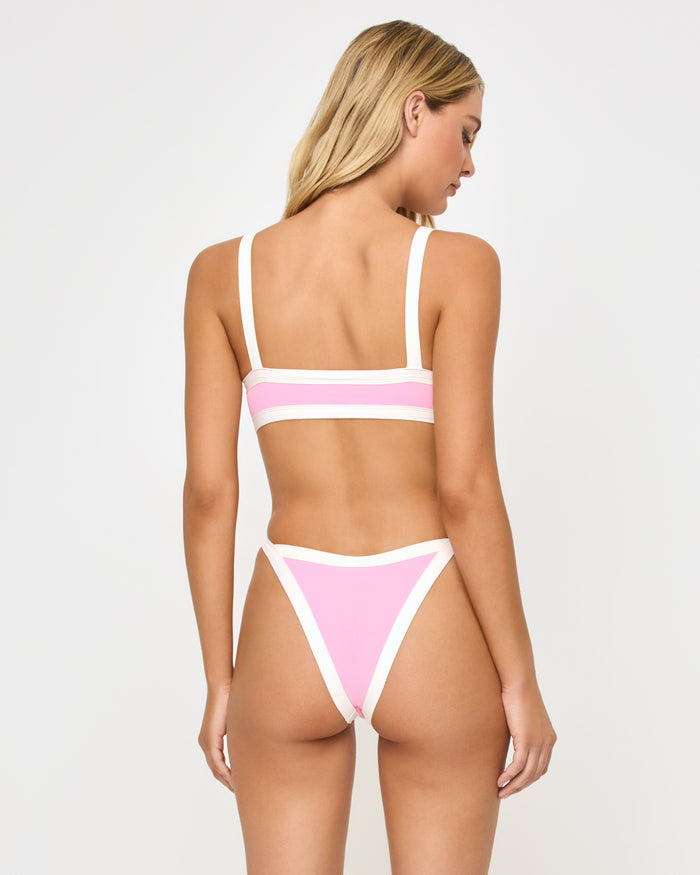 Back view of a model wearing the LSPACE pink sugar cream Mackenzie Bikini Bottom with cream contrast trim piping, showing the pink ribbed fabric, paired with a matching Taylor Bikini Top.
