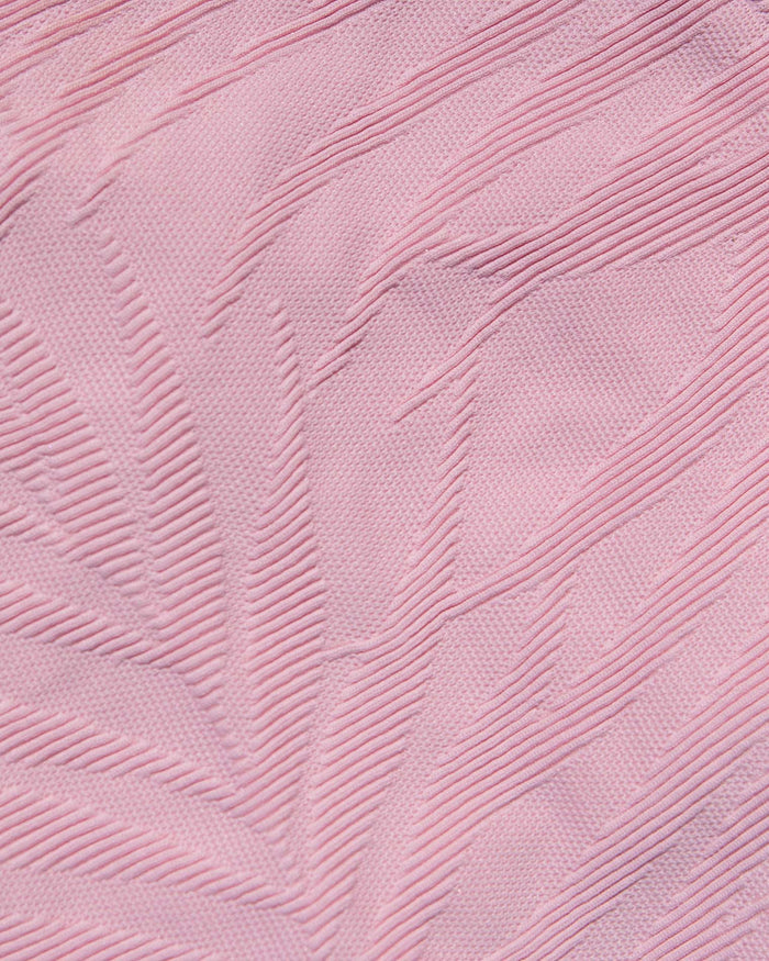 A close-up of light pink textured fabric with a raised leaf-like pattern.