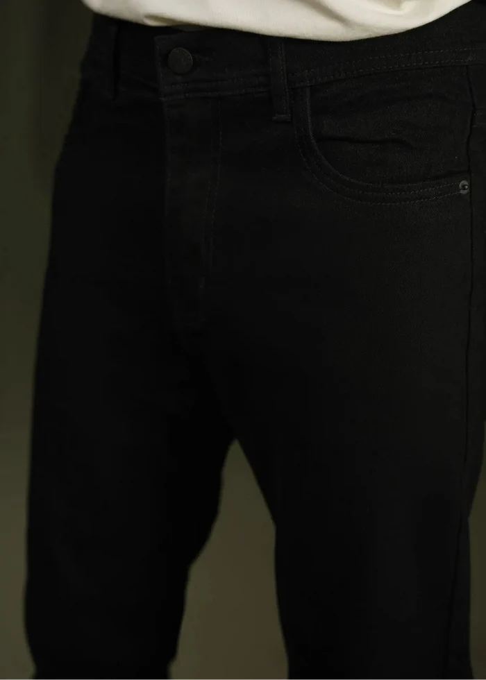 Black chino pants waist close-up: button fly, belt loops, and side pocket detail.