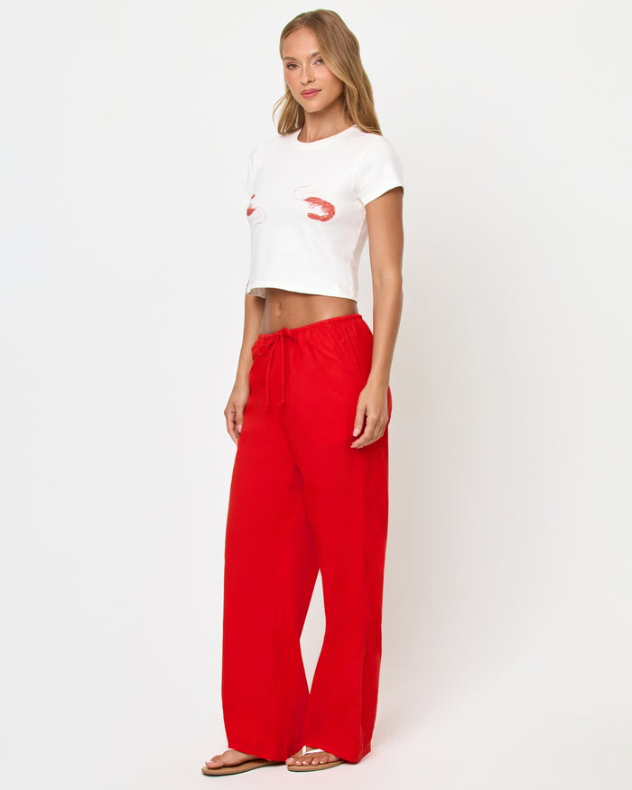 Three-quarter side view of a model wearing the LSPACE Merci Baby Tee in Shrimp, showing the cropped silhouette with shrimp graphics partially visible, styled with red wide-leg drawstring pants.