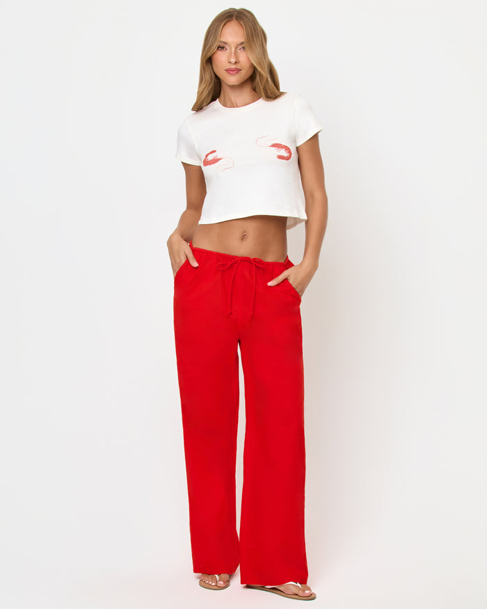Front view of a model wearing the LSPACE Merci Baby Tee in Shrimp, showing the full-length look with coral-red shrimp graphics on the white cropped tee, styled with red wide-leg drawstring pants.