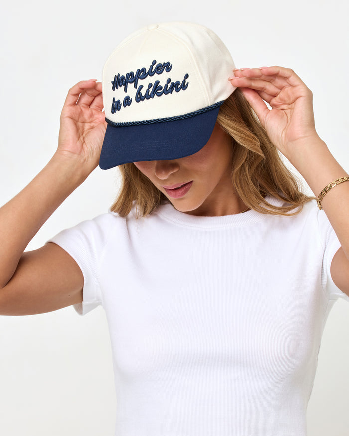 Front view of a model looking down with hands on the brim of the midnight cream Newport Hat.