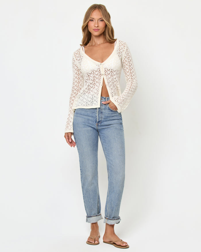 Front view of a model wearing the LSPACE Nova Top in cream, showing the long-sleeve crochet top with deep V-neckline and open tie-front, styled with light wash jeans.
