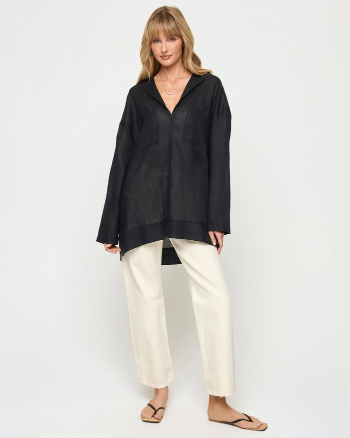 Front view of a model wearing the LSPACE Oasis Tunic in black, featuring an open V-neckline with collar, long sleeves, and a relaxed oversized silhouette, styled with cream wide-leg pants.