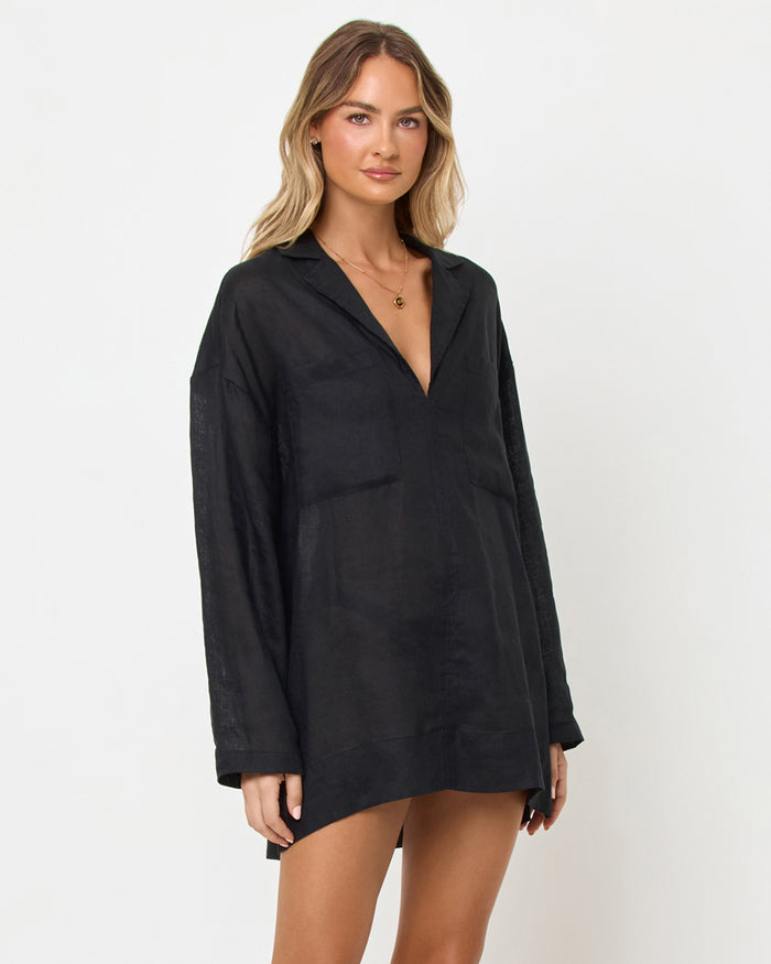 Three-quarter view of a model wearing the LSPACE Oasis Tunic in black as a cover-up, featuring an open V-neckline with collar, long sleeves, and a relaxed oversized silhouette.