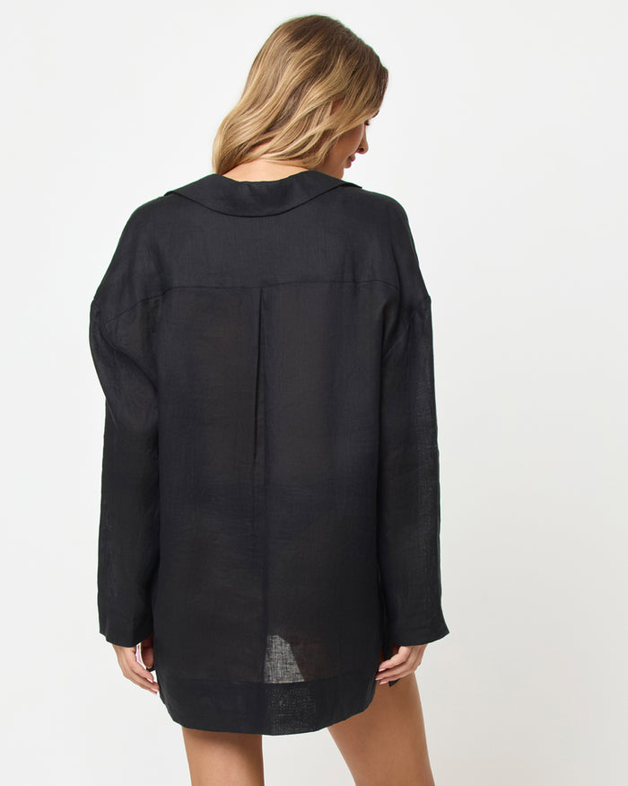Back view of a model wearing the LSPACE Oasis Tunic in black as a cover-up, showing a collared neckline, long sleeves, a center back panel, and a relaxed oversized silhouette.