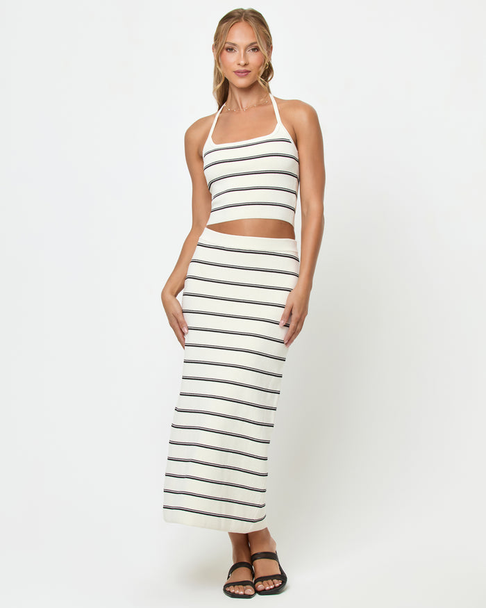 Front view of a model wearing the LSPACE Positano Top in mykonos stripe, a cropped halter top with a square neckline and cream and black horizontal stripes, styled with the matching Ravello Skirt.