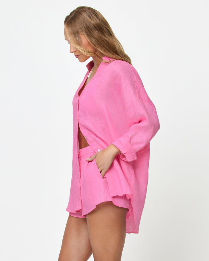 Side view of a model wearing the LSPACE Rio Tunic in hottest pink, an oversized linen button-up shirt with a relaxed fit and three-quarter sleeves, styled with the matching Rio Short.