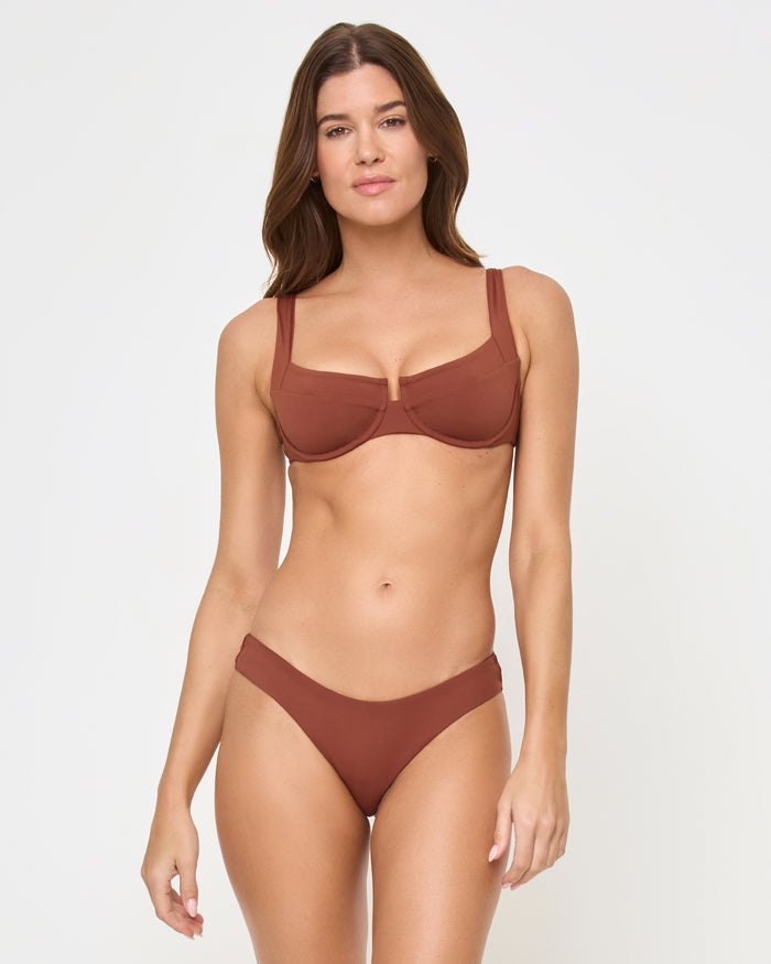 Front view of a model wearing the LSPACE Tobacco Rocky Bikini Bottom, a mid-rise bikini bottom in warm rust-brown, paired with a matching tobacco underwire bralette Mako Bikini Top with center front keyhole detail.