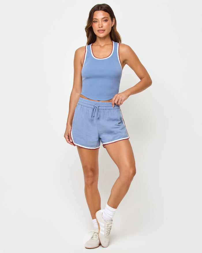 Cream Chambray Fig | Badge:New Arrival_#B2AC88_#ffffff'

Front full-length studio view of the Ash Tank and Rune Short in Cream-Chambray-Fig, a chambray blue ribbed scoop-neck crop tank with white and burgundy crochet trim paired with matching chambray blue runner shorts with the same crochet trim, white crew socks, and cream sneakers.