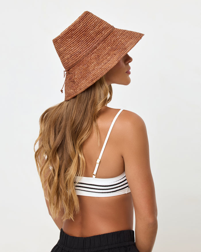 Back view of a model wearing the brown Seville Hat with a white and black striped bikini top and black shorts.