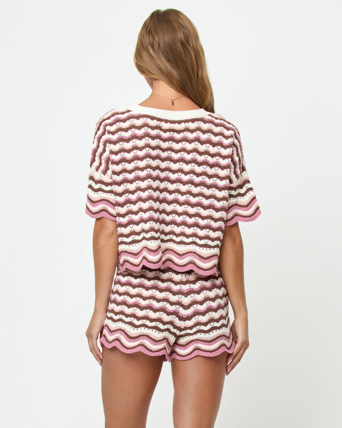 Back view on model of the LSPACE Sunchaser Top in Neapolitan, a short-sleeve crochet top in a brown, pink, and white wave pattern with scalloped hem, styled as a set with the matching Sunchaser Short.