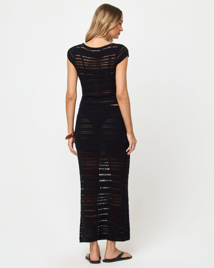 Back view of model wearing the LSPACE Tula Top in black, a semi-sheer crochet cropped top with the matching Skirt.